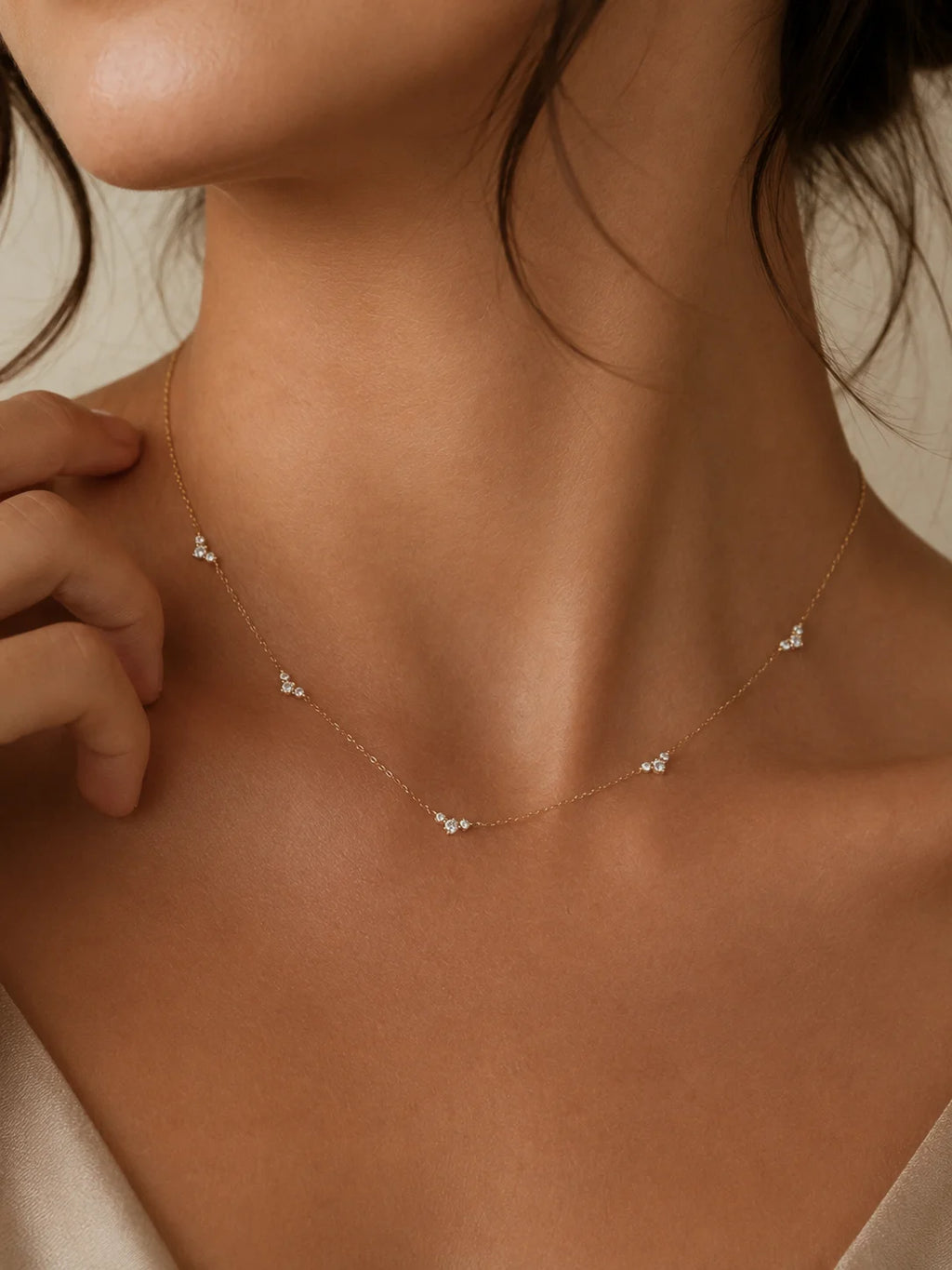 A delicate gold chain necklace with small, clear crystal butterfly charms worn by a model. The shot is a close-up of the model's neck and upper chest, highlighting how the fine chain drapes against the skin.
