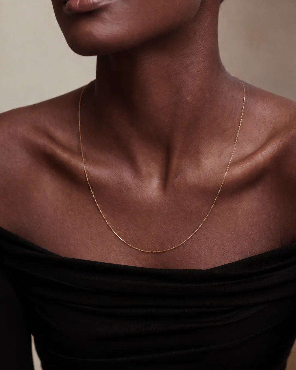 Close-up of a person wearing a delicate gold necklace against a neutral background