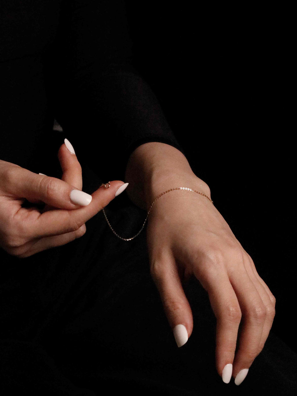 Close-up of hands with a delicate bracelet on a black background