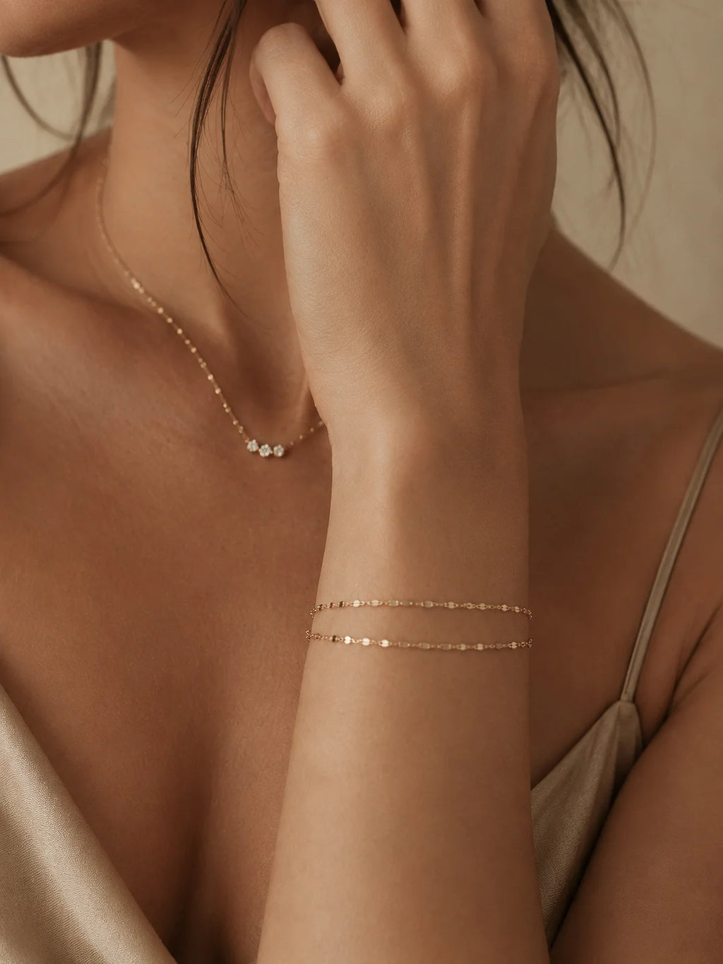 A close-up lifestyle shot of a model wearing delicate rose gold jewelry, featuring a double-strand beaded bracelet on her wrist and a matching fine chain necklace with small white beads.