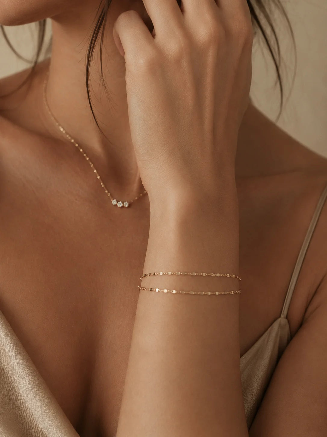 A close-up lifestyle shot of a model wearing delicate rose gold jewelry, featuring a double-strand beaded bracelet on her wrist and a matching fine chain necklace with small white beads.