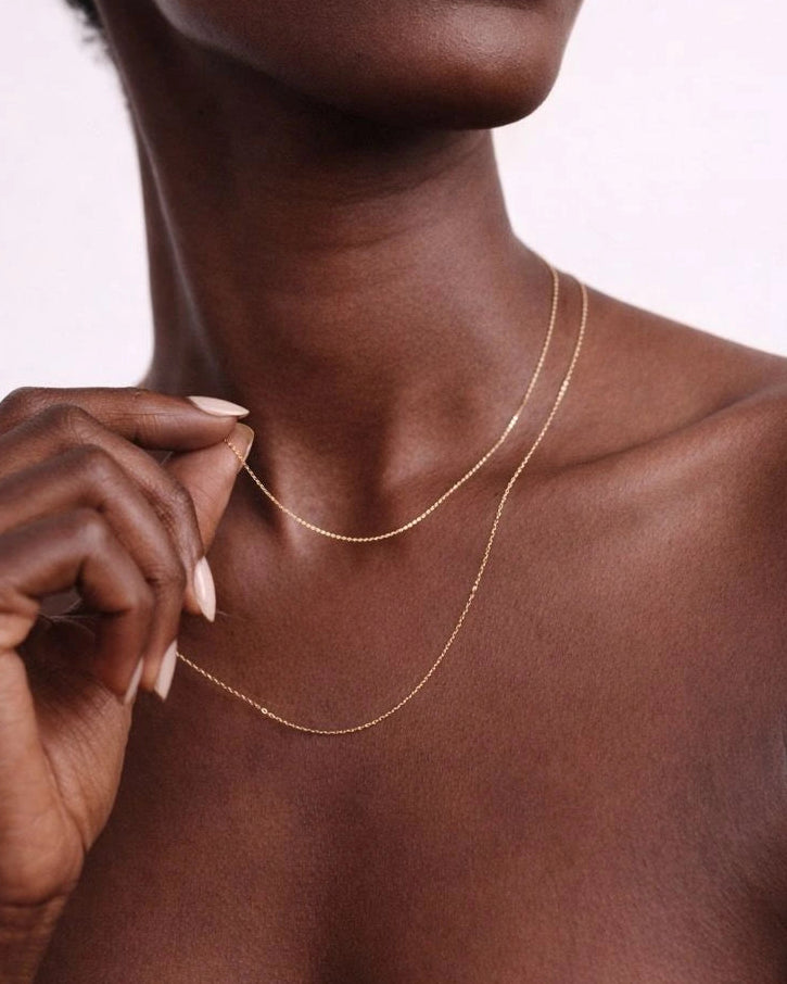 Close-up of a person wearing a delicate gold necklace against a neutral background