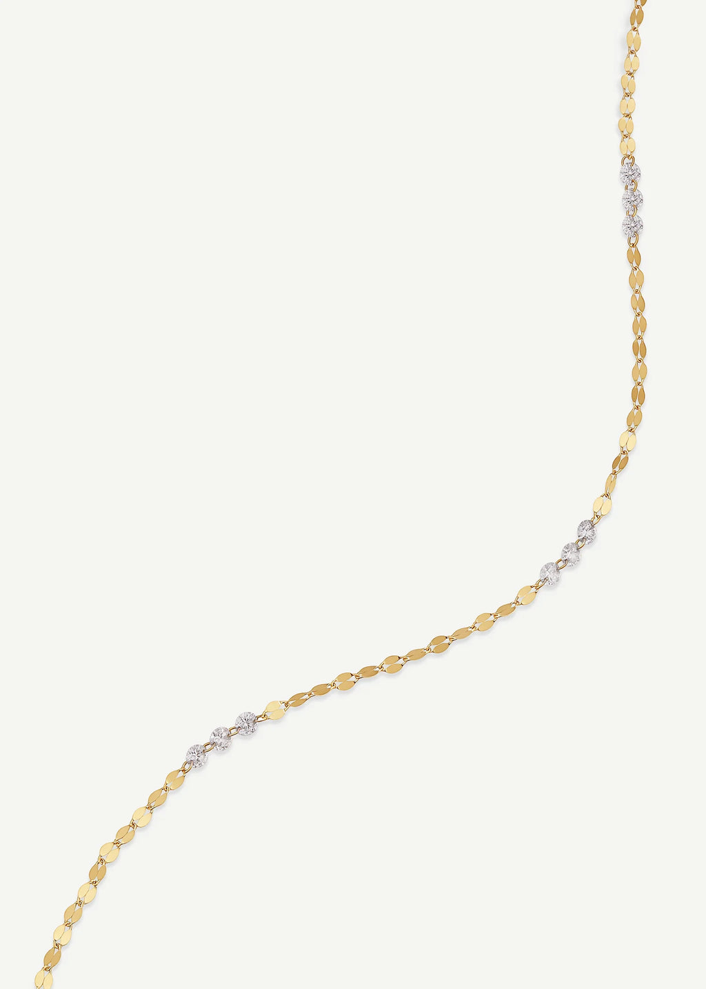 A delicate gold chain necklace featuring a series of small clear gemstones set in alternating gold and silver-toned metal links, displayed on a light off-white background.