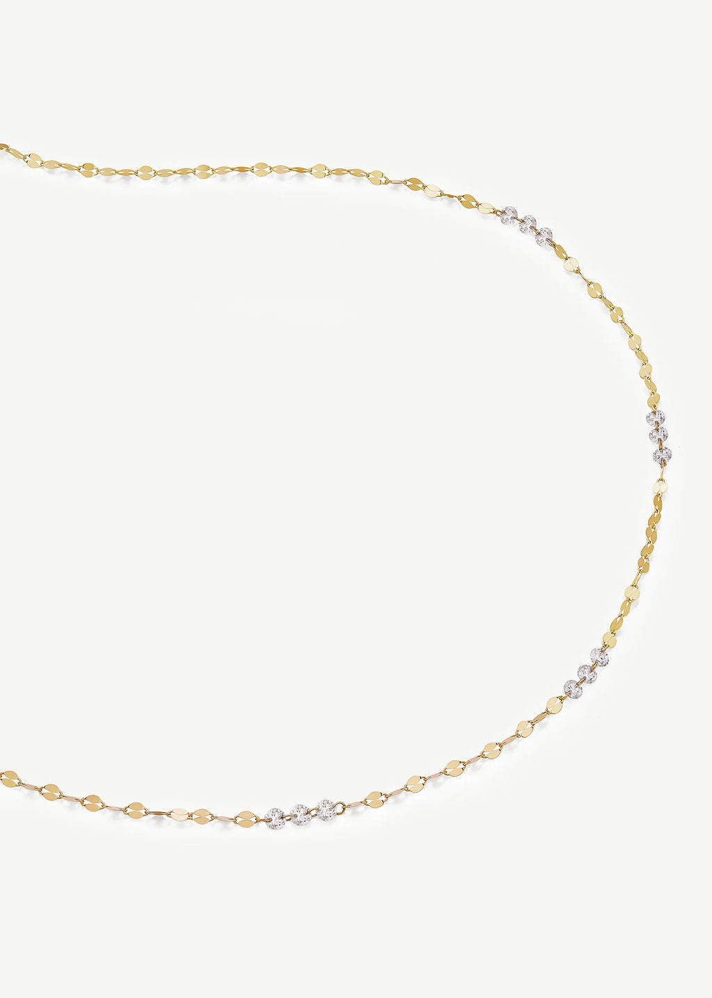 A delicate gold chain necklace with a small section of clear cubic zirconia stones set in yellow gold, displayed on a light cream background.