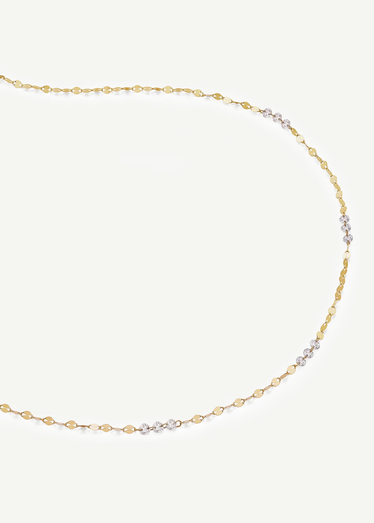 A delicate gold chain necklace with a small section of clear cubic zirconia stones set in yellow gold, displayed on a light cream background.