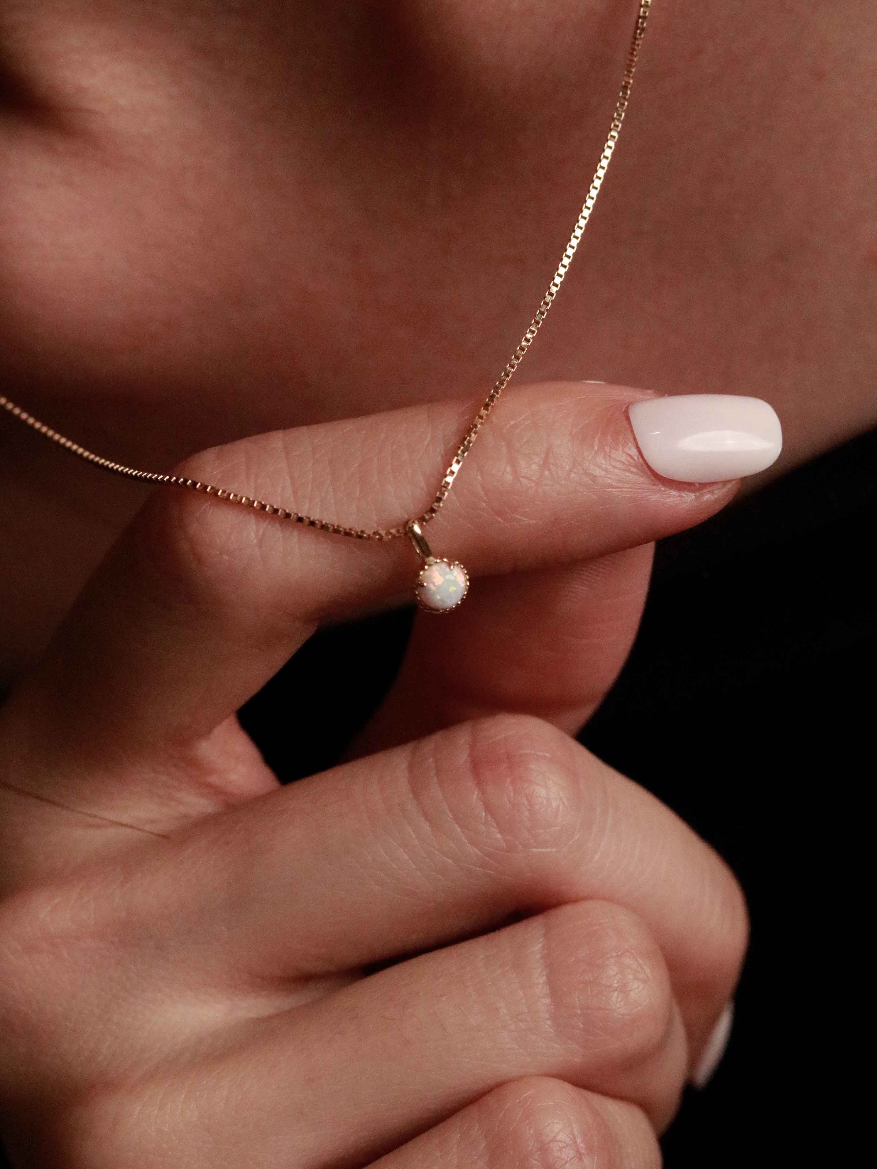 Close-up of a hand wearing a delicate gold box chain necklace with a small white opal