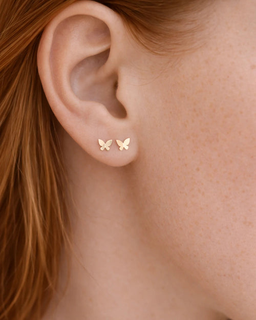 Close-up of a person wearing gold butterfly earrings.