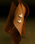 Butterfly-shaped earrings on a brown leaf against a dark background