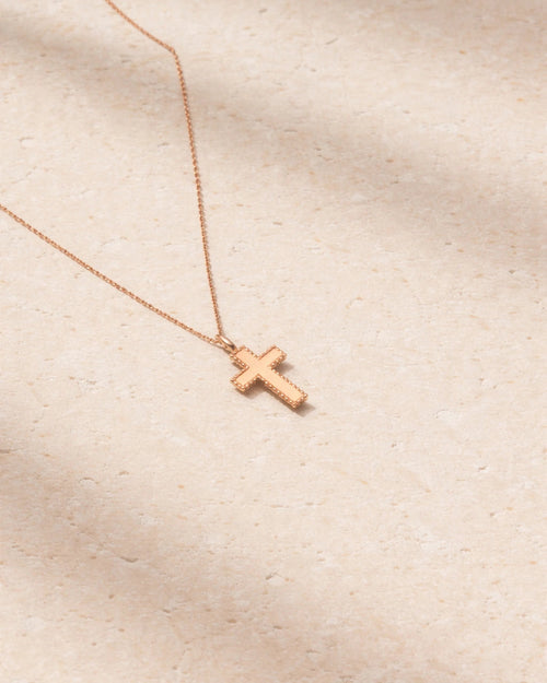 Rose gold cross necklace on a beige fabric background