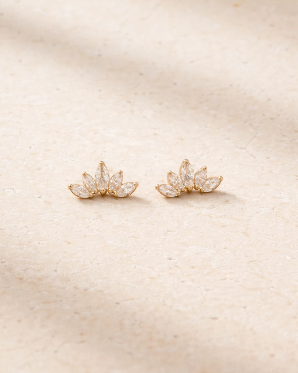 Pair of gold earrings with a floral design on a beige background