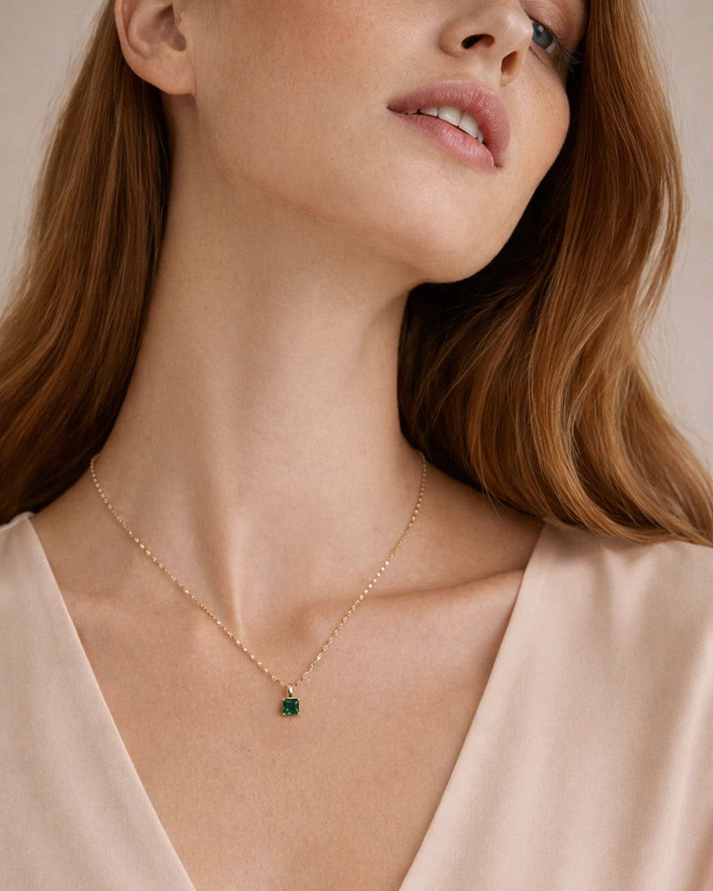 Close-up of a woman wearing a gold necklace with a green pendant against a neutral background