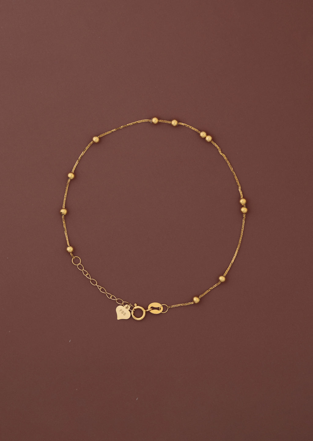 18K solid gold satellite bead station bracelet full view on dark burgundy background, FSS heart charm tag and spring ring clasp visible, hallmarked au750