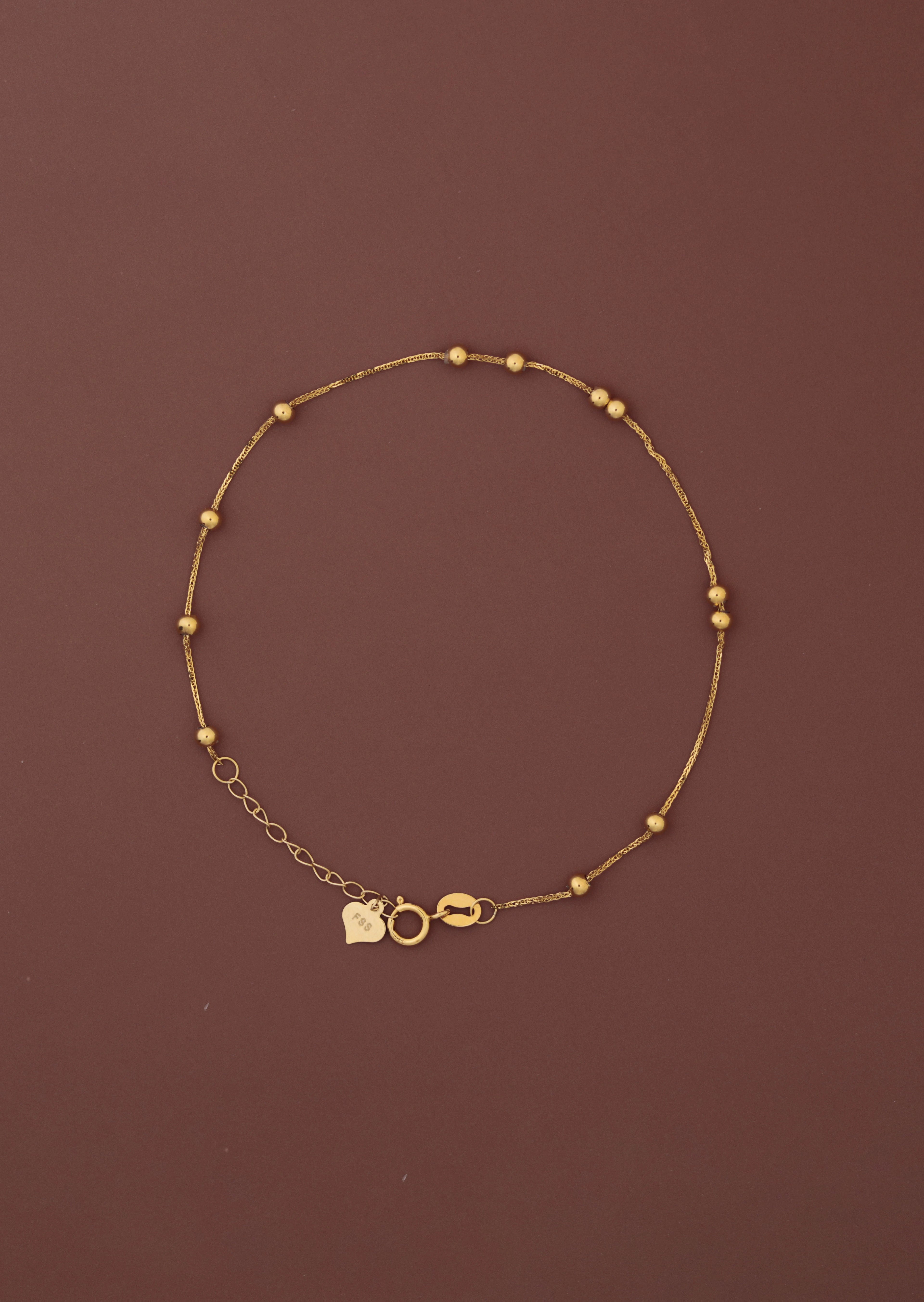 18K solid gold satellite bead station bracelet full view on dark burgundy background, FSS heart charm tag and spring ring clasp visible, hallmarked au750