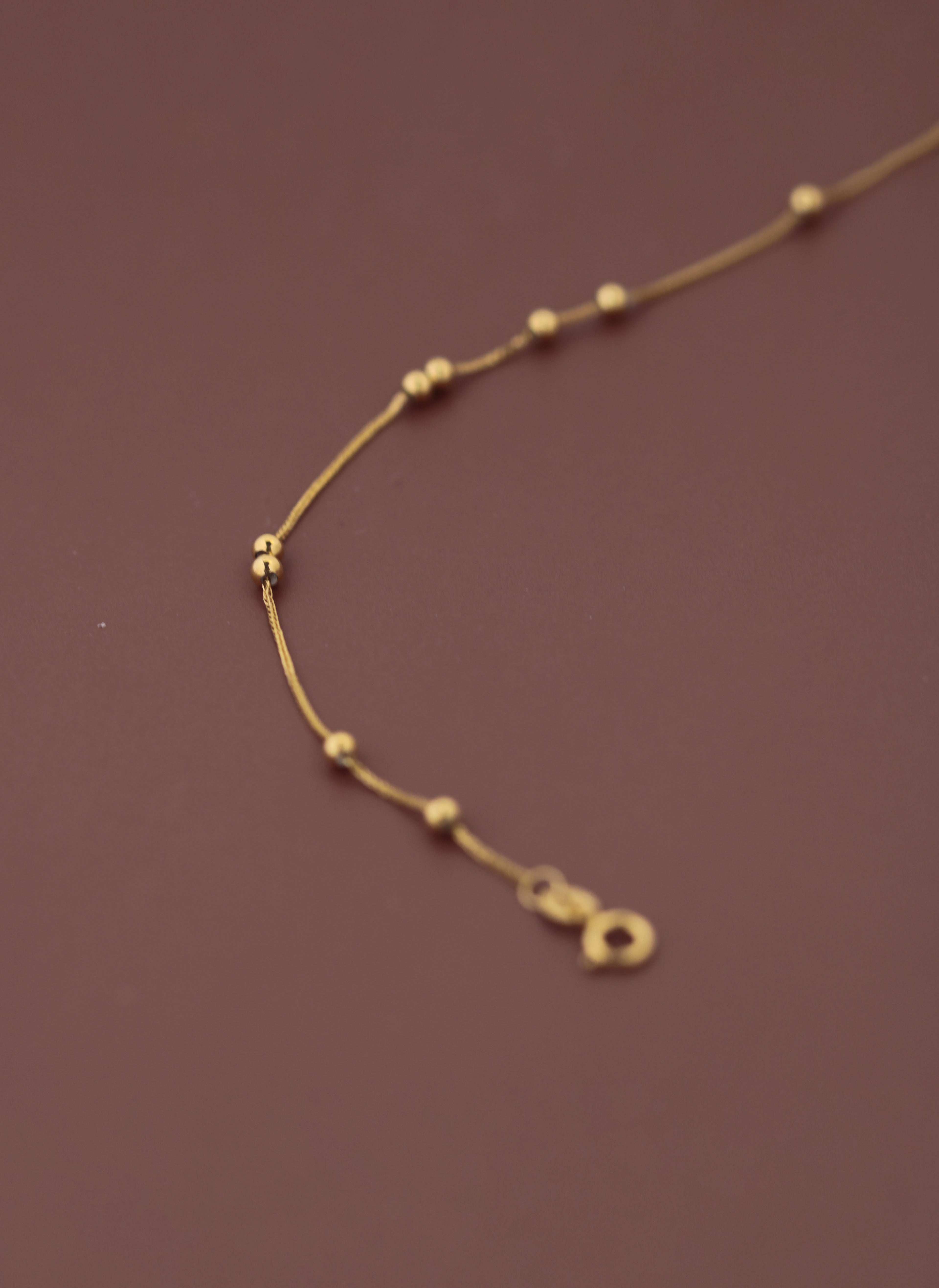 Close-up of 18K solid gold bead bracelet clasp and extension chain on burgundy background, showing spring ring closure and FSS hallmark tag, hallmarked au750