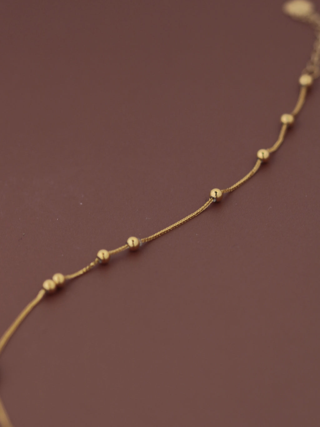  length18K solid gold satellite bead bracelet laid flat on dark burgundy background, showing evenly spaced gold ball stations and fine chain links