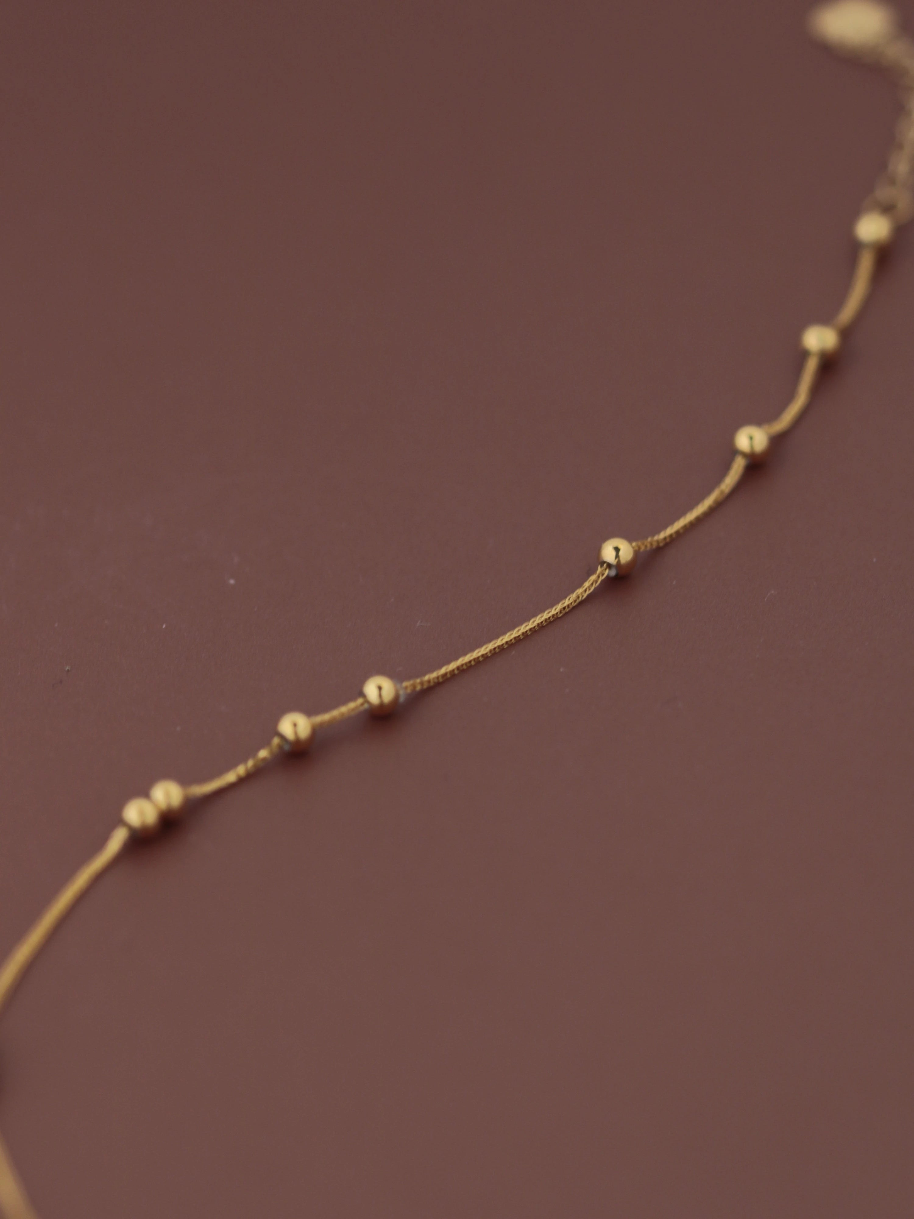  length18K solid gold satellite bead bracelet laid flat on dark burgundy background, showing evenly spaced gold ball stations and fine chain links