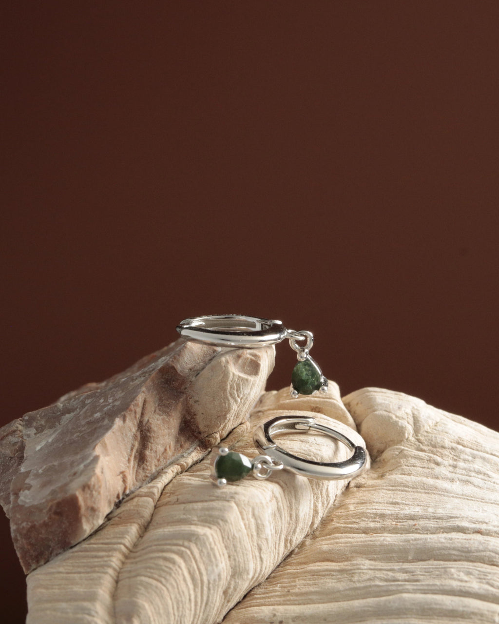 Silver rings with green gemstones on a wooden surface