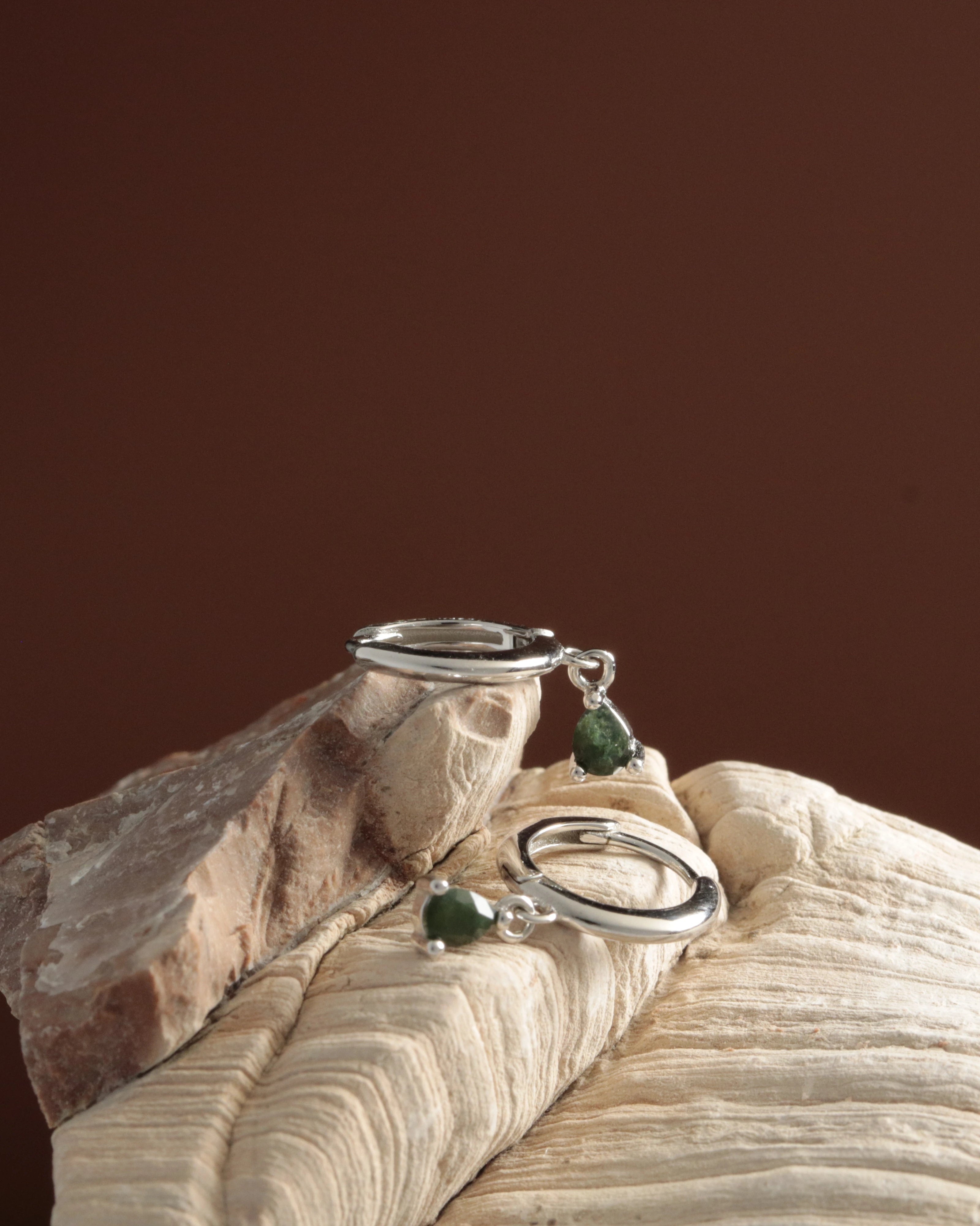 Silver rings with green gemstones on a wooden surface