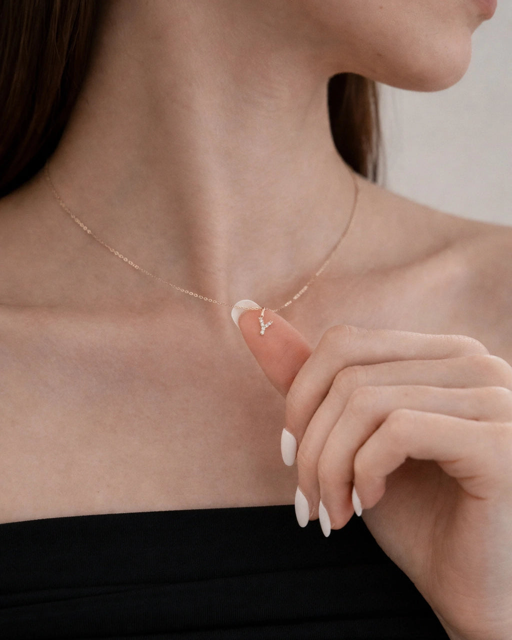 Woman wearing a delicate necklace with a small pendant, holding her hand near her neck.