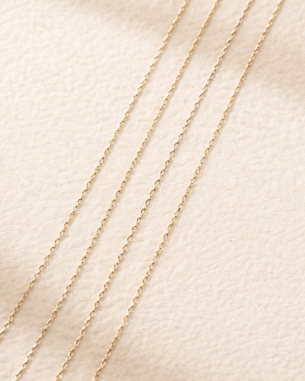 Three gold chains of different lengths on a beige fabric background