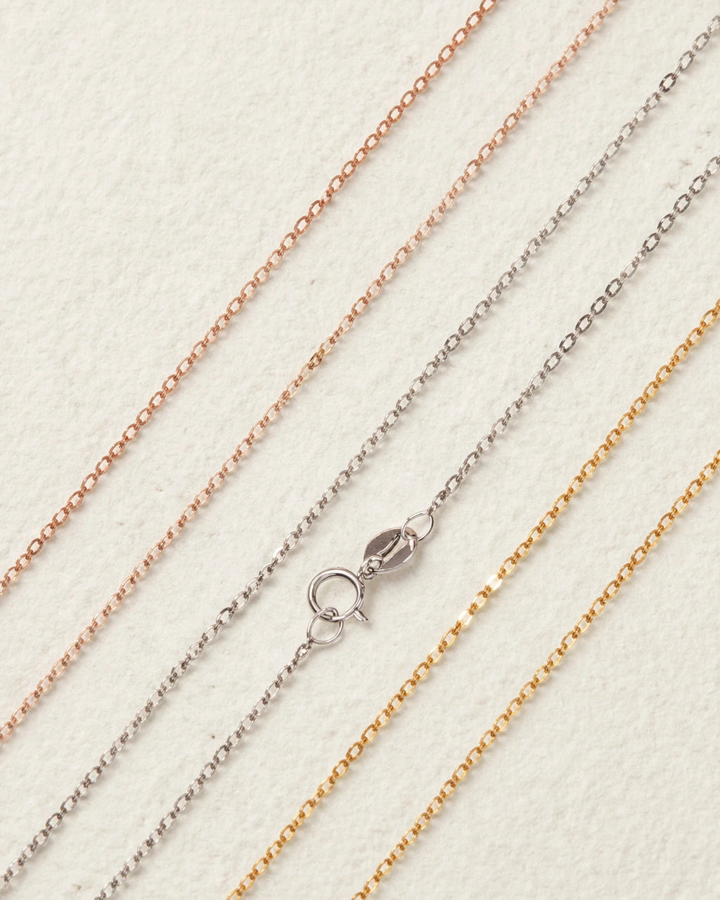 Three gold chains of different colors on a light background