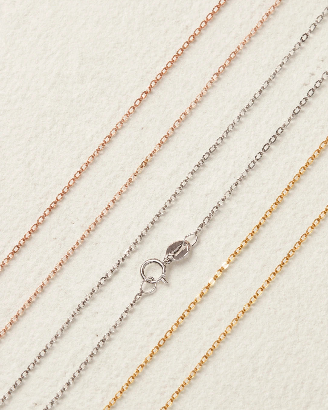 Three gold chains of different colors on a light background