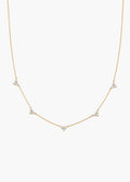 A delicate gold chain necklace featuring five small triangular clusters of clear stones, displayed against a solid off-white background.