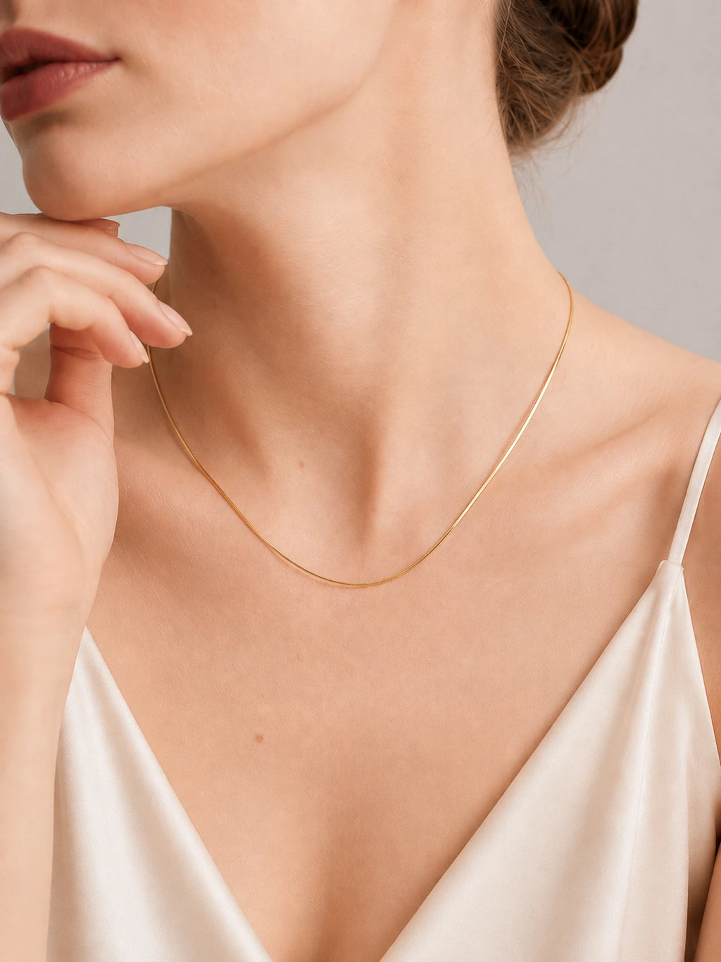  2Woman wearing dainty 18K solid gold snake chain necklace at collarbone length, yellow gold flat links, styled with blush silk slip dress