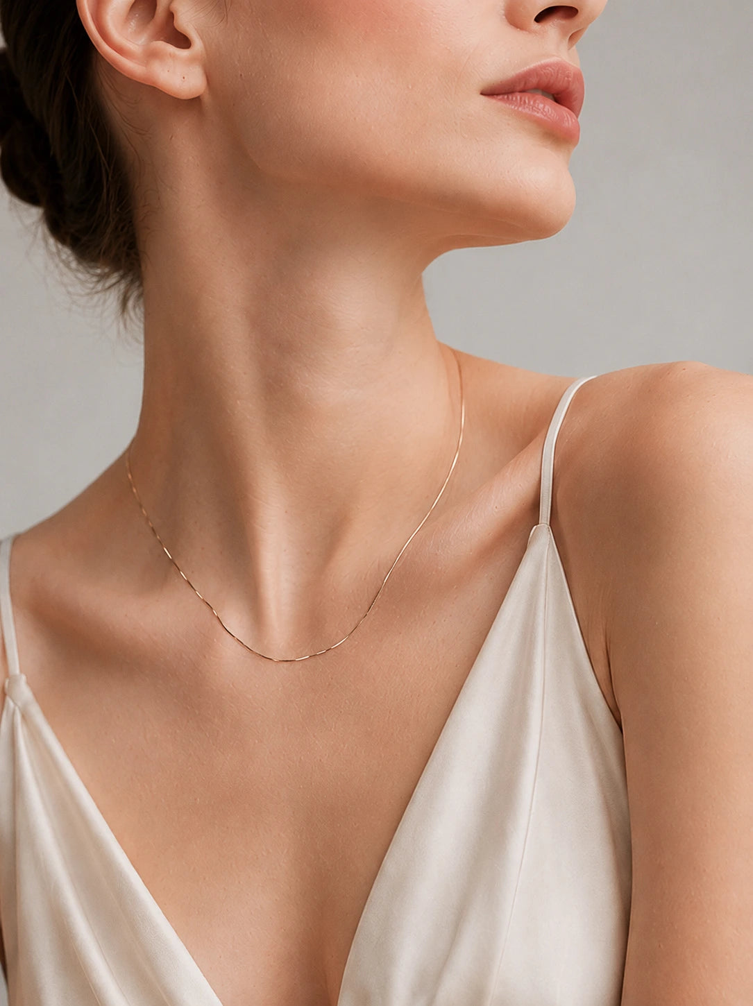 18K solid gold snake chain necklace worn close to the neck on model in cream satin dress, side profile, neutral grey background