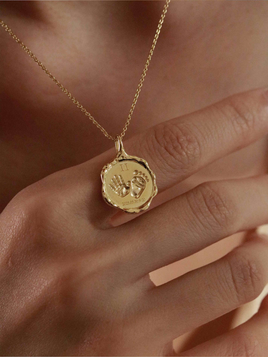 Gold necklace with a pendant engraved with baby hands 