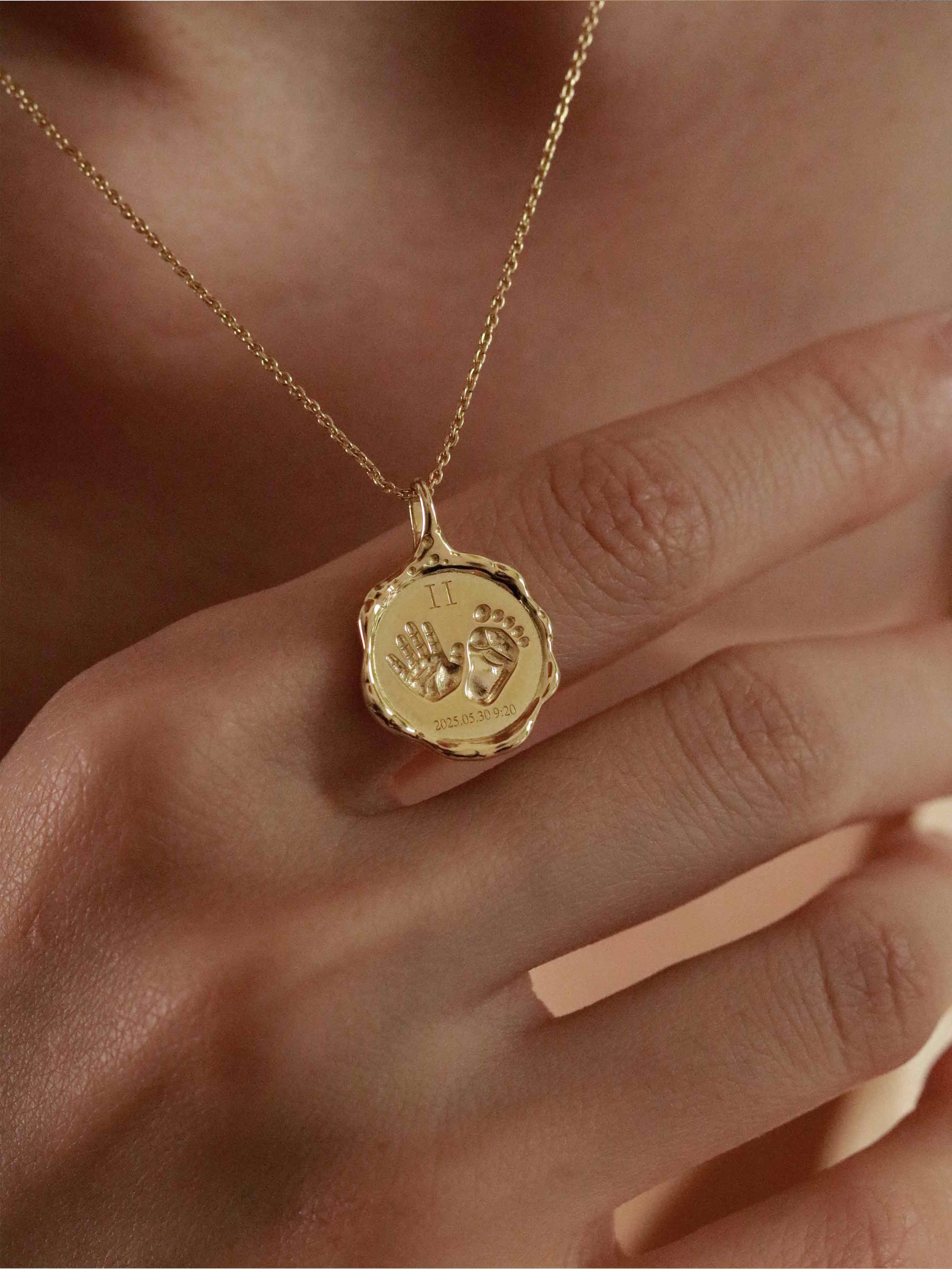 Gold necklace with a pendant engraved with baby hands 