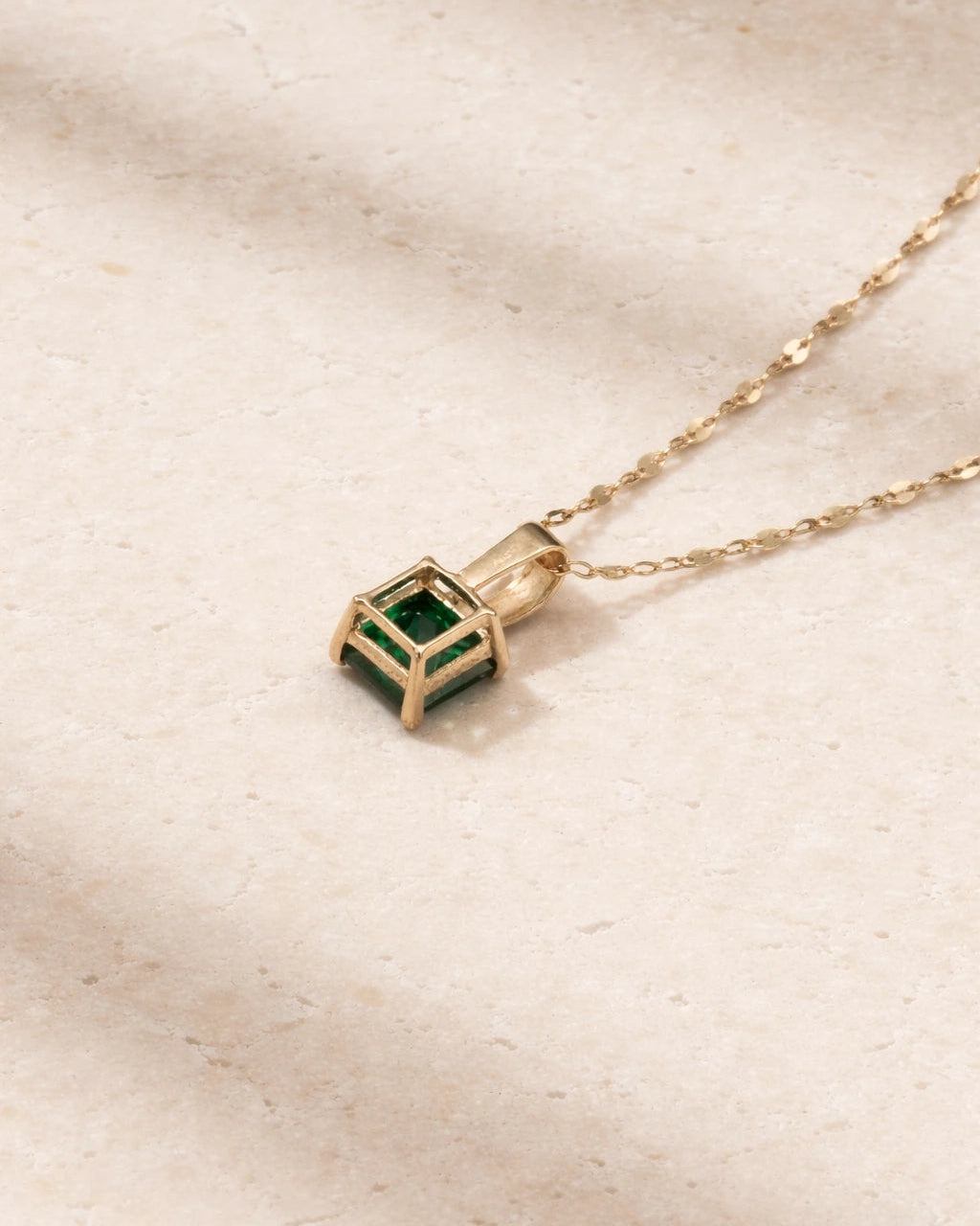 Gold necklace with a green gemstone pendant on a beige background