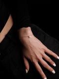 Hand wearing a delicate bracelet with a small round charm on a dark background