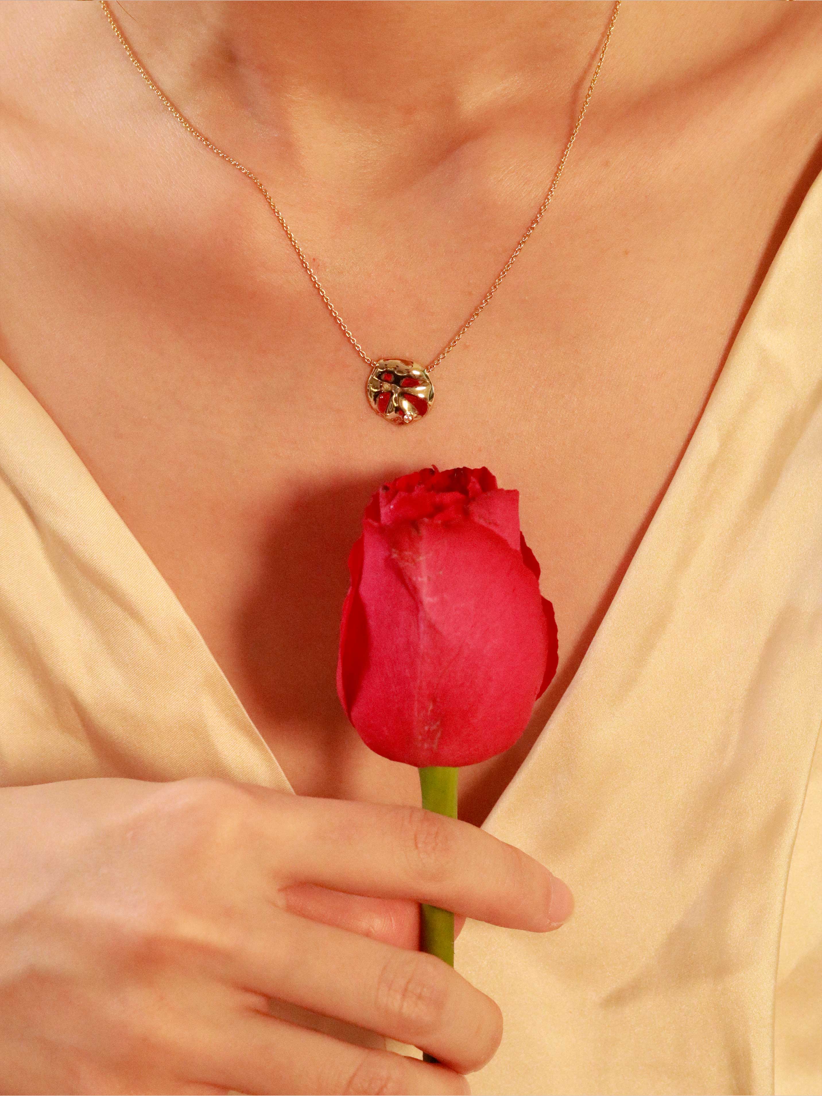 Red tulip held by a hand with a gold necklace featuring a pendant.