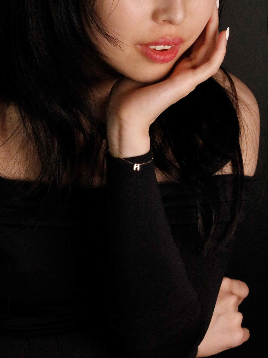 Woman wearing a black dress with a delicate gold bracelet against a dark background