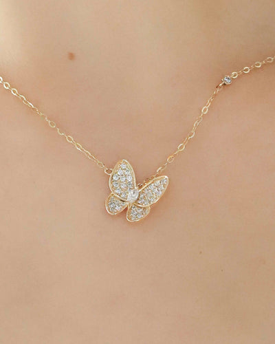 Gold butterfly necklace on a person's neck against a neutral background