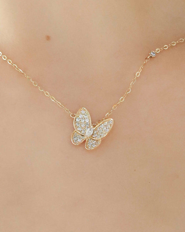Gold butterfly necklace on a person's neck against a neutral background