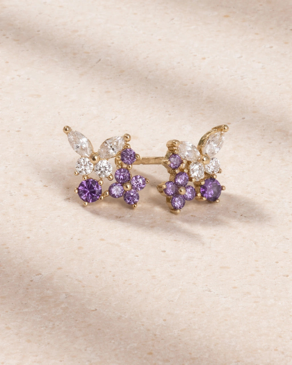 Gold and purple floral earring on a beige background