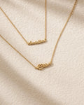 Gold nameplate necklace on a textured beige surface