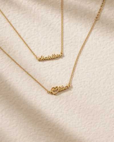 Gold nameplate necklace on a textured beige surface
