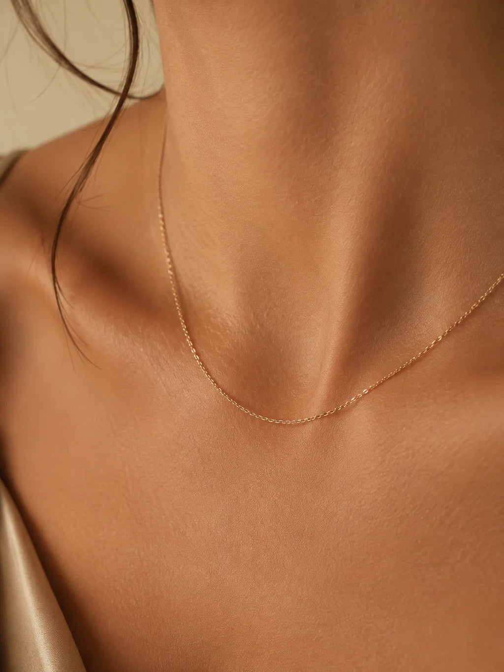A delicate rose gold chain necklace worn on a model's neck, shown in a close-up shot with warm, soft lighting.