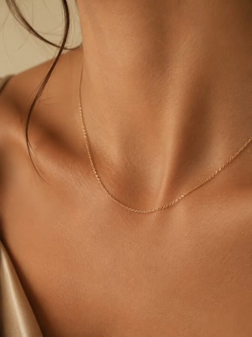 A delicate rose gold chain necklace worn on a model's neck, shown in a close-up shot with warm, soft lighting.