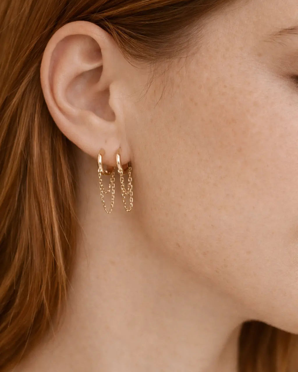 Close-up of a person wearing gold hoop earrings with red hair.