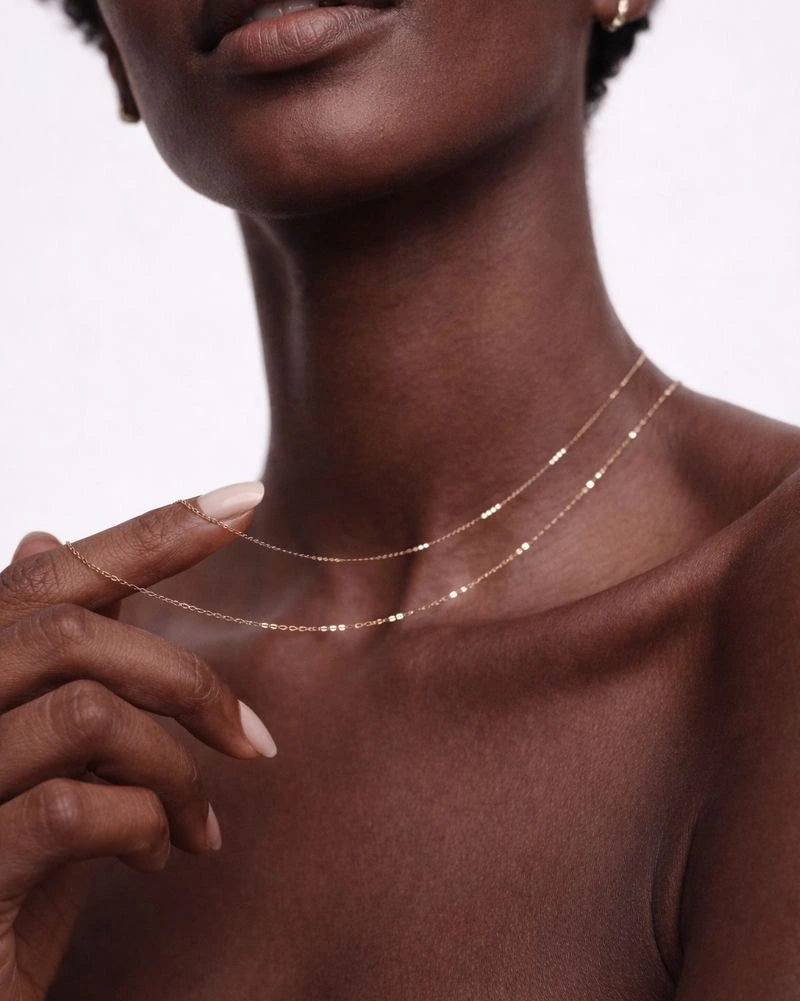 Close-up of a woman wearing a delicate gold necklace against a neutral background