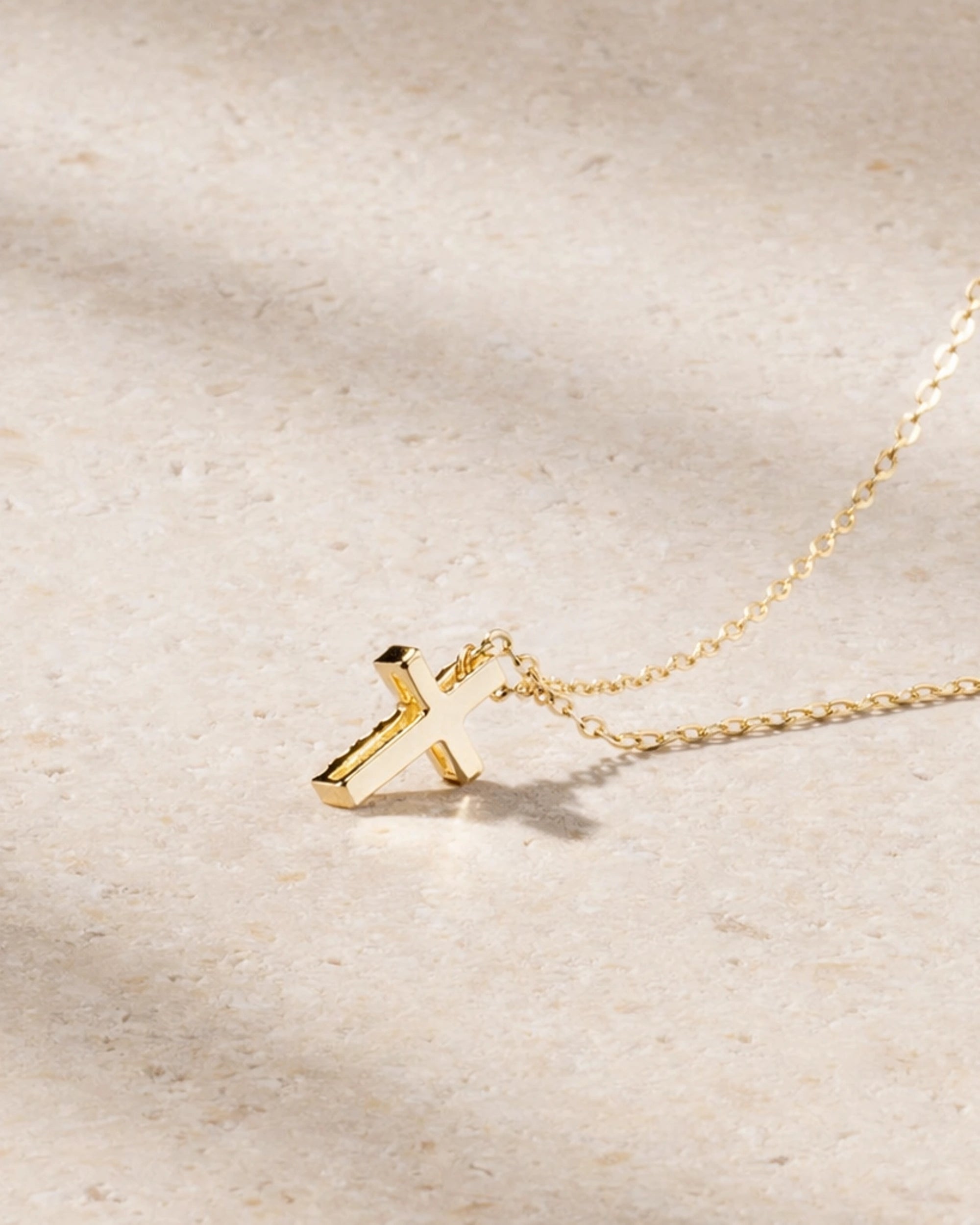 Gold necklace with a small cross pendant on a beige background