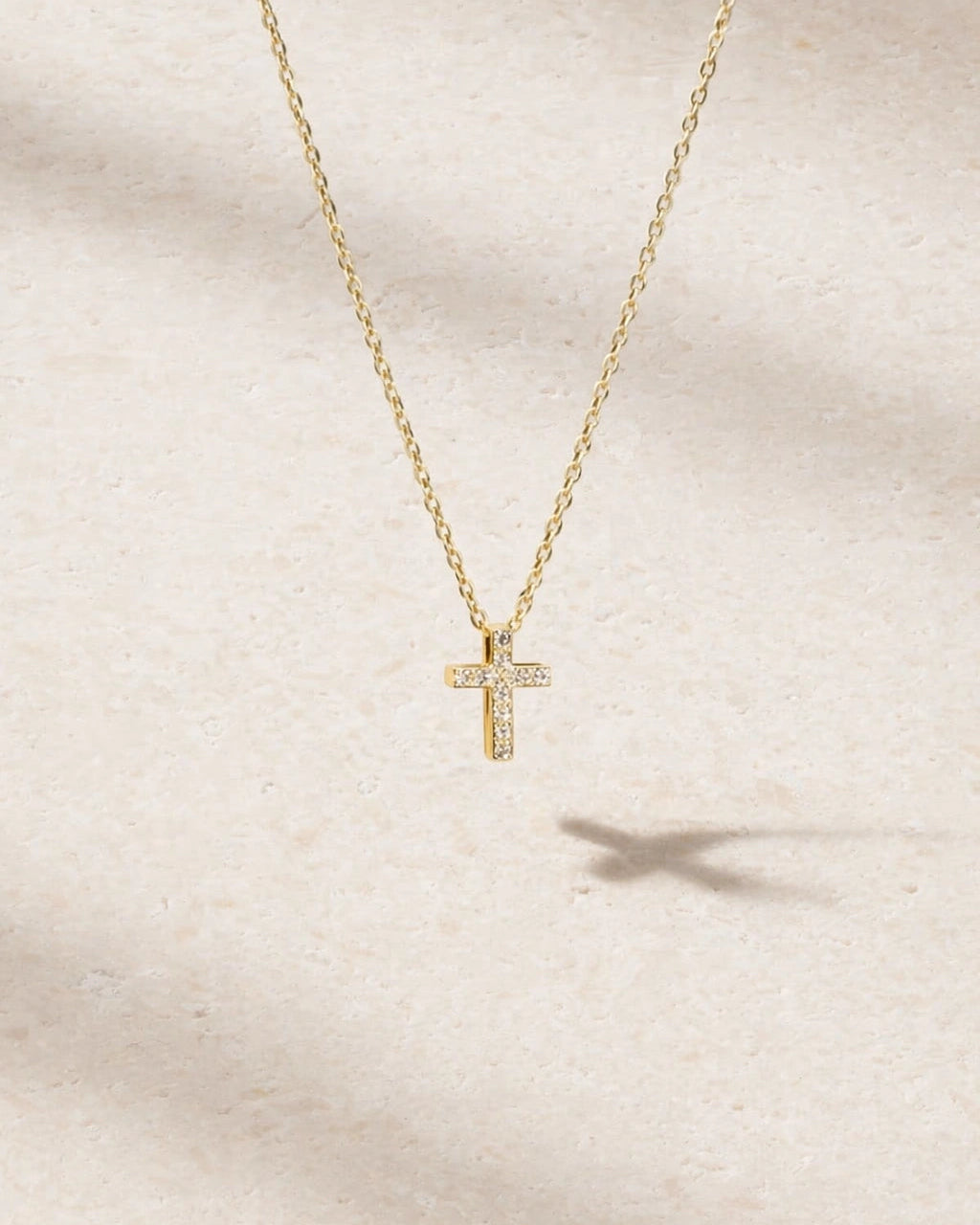 Gold cross necklace with diamonds on a beige background