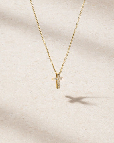Gold cross necklace with diamonds on a beige background