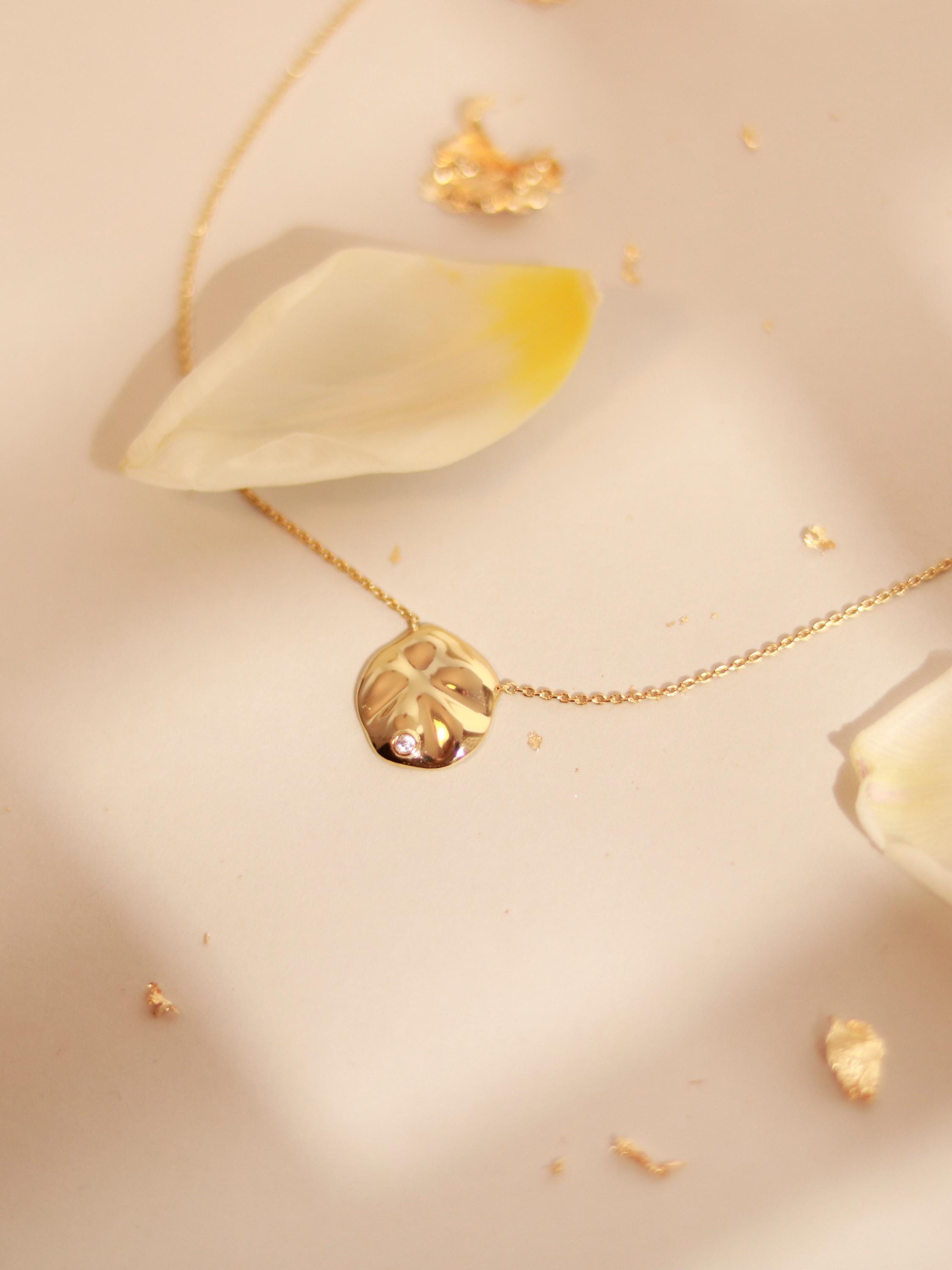 Gold necklace with a leaf-shaped pendant on a light beige background