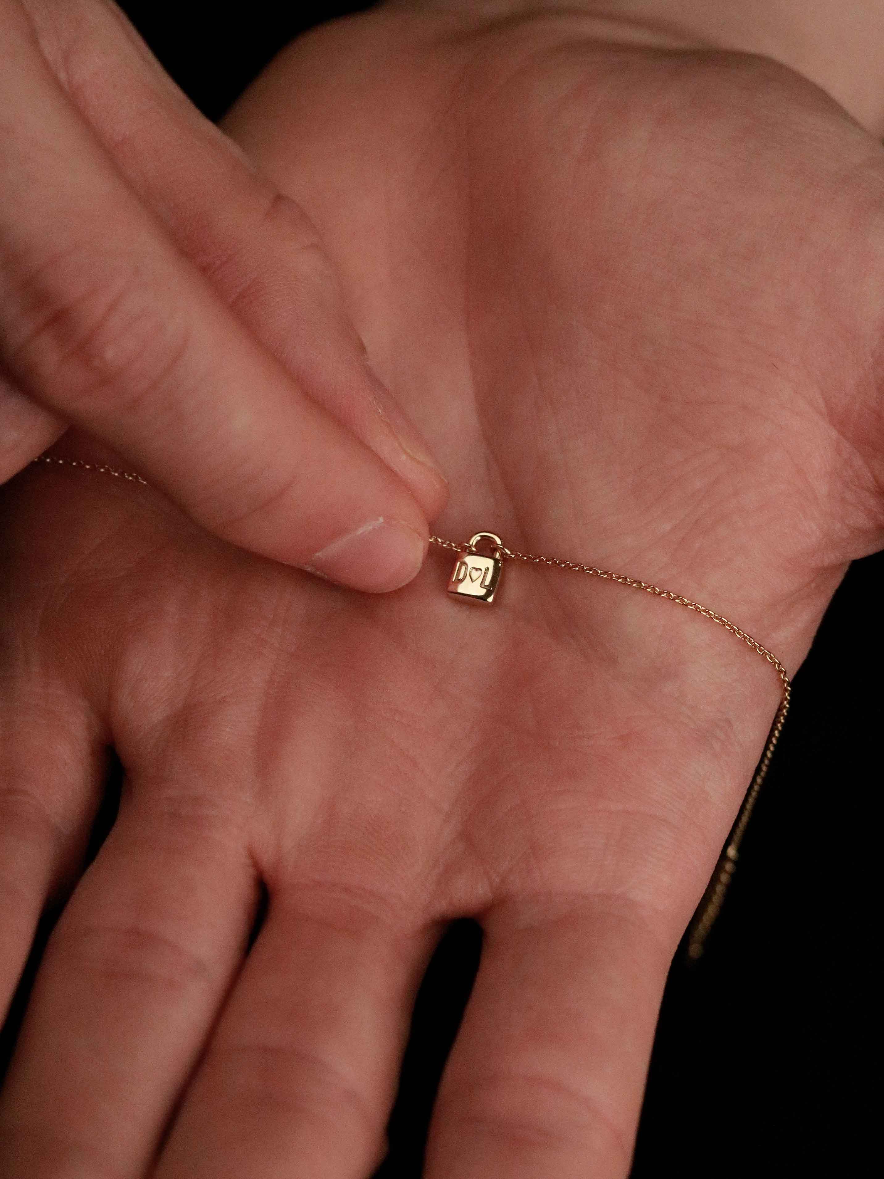 Gold bracelet with a lock charm on a hand against a dark background taking the bracelet