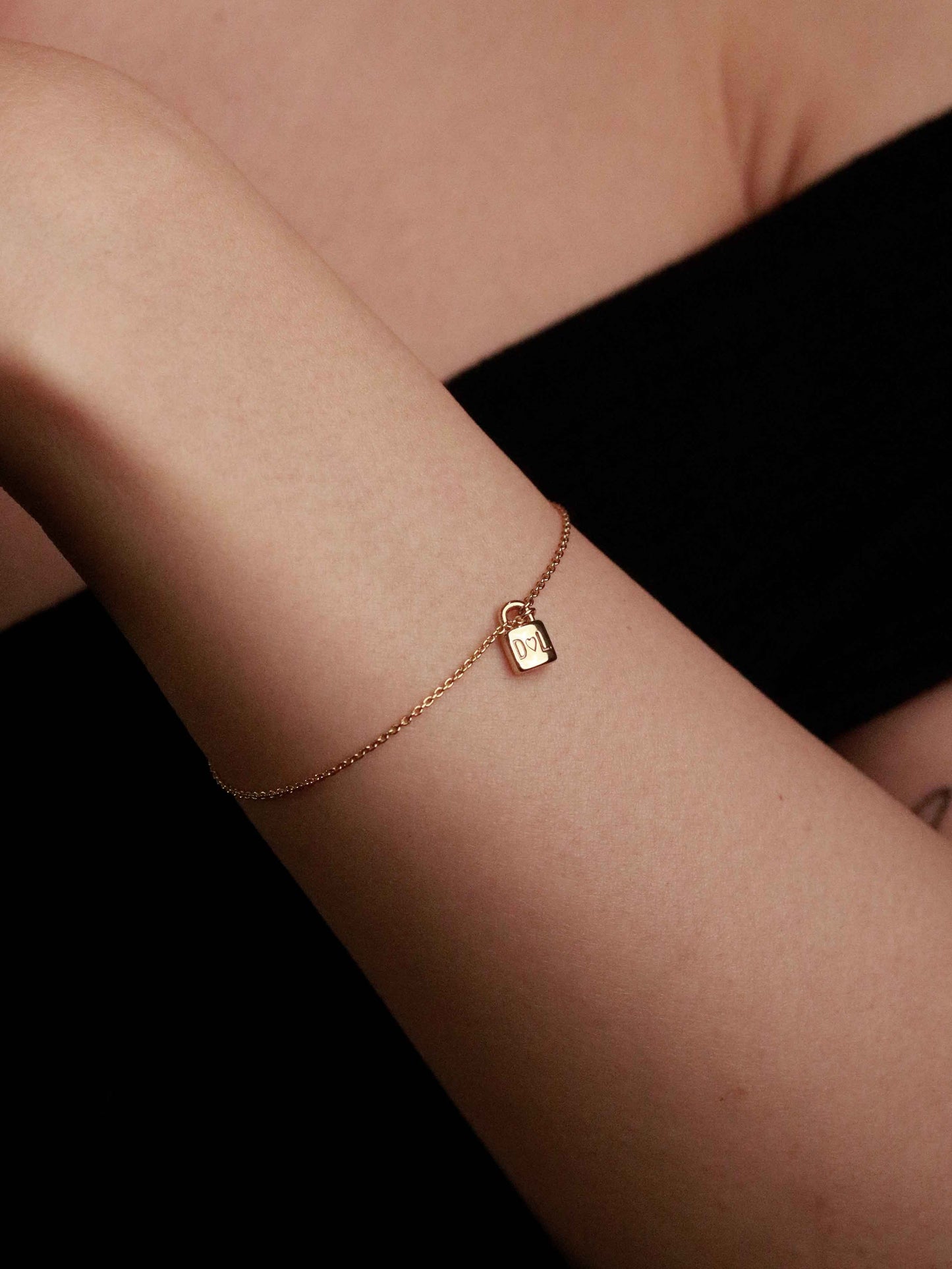 Gold bracelet with a small lock charm on a person's wrist against a dark background